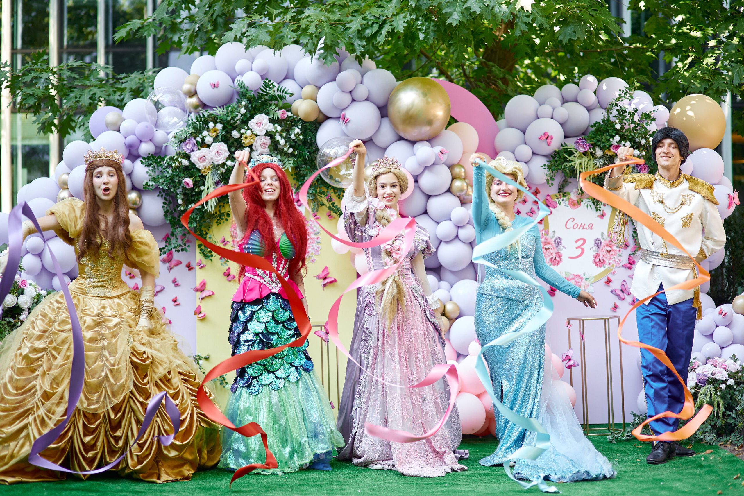 Group of princess and prince performers waving colorful ribbons on stage at a children’s event.