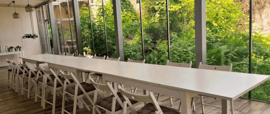 Bright minimalist event room with a long white table and large windows facing greenery.