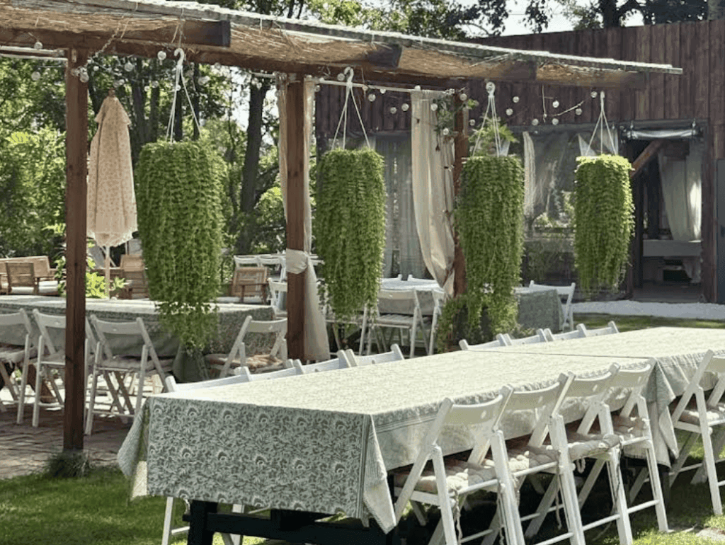 Outdoor event space with garden tables, hanging plants, and rustic wooden pergola perfect for family gatherings or summer parties.