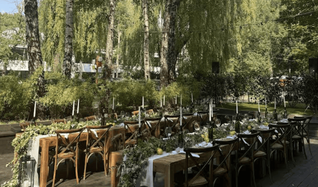 Outdoor garden banquet setup surrounded by trees and natural foliage.