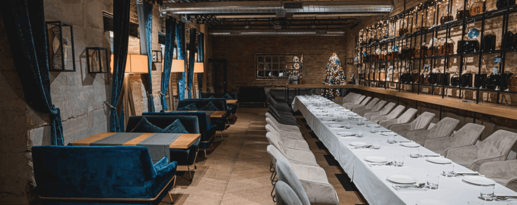 Elegant restaurant hall decorated with blue velvet curtains, festive lights, and a long banquet table for celebrations.