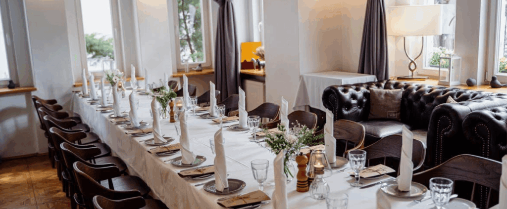 Classic European-style restaurant with a long white banquet table, cozy leather sofas, and intimate event lighting.